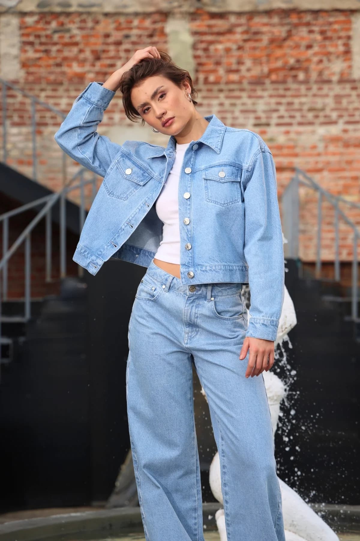 Denim Moon kadın açık mavi yıkamalı önden düğmeli crop oversize denim ceket, modelde eli saçında önden görünüm.