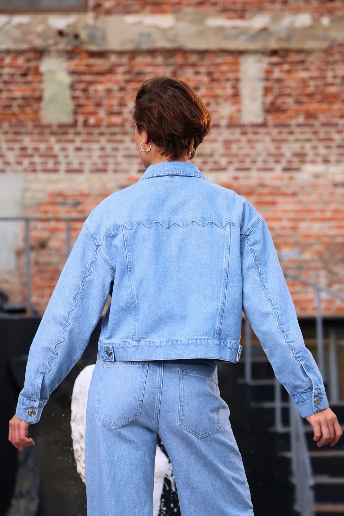 Denim Moon women's light wash cropped denim jacket, full back view with wavy seam detail along sleeves and back.